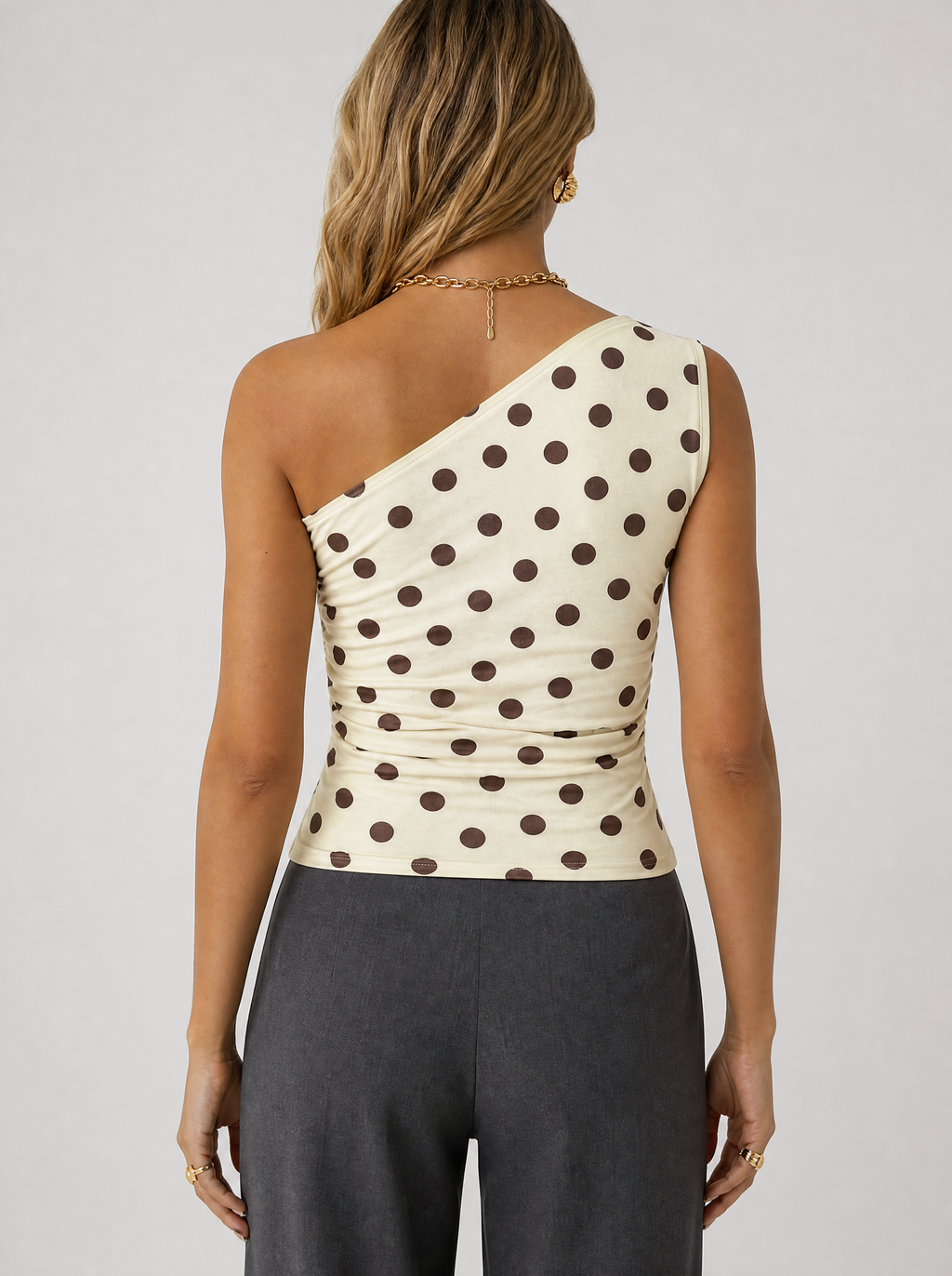 Back view of a cream polka dot one shoulder top showing the asymmetric shoulder line