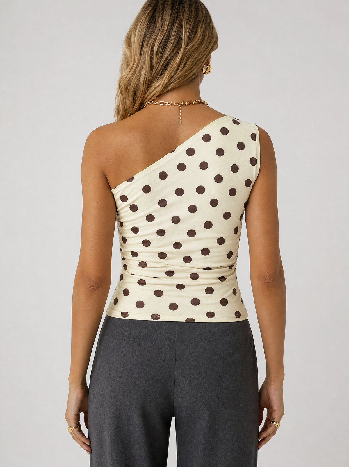Back view of a cream polka dot one shoulder top showing the asymmetric shoulder line