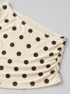 Close up of the asymmetric neckline and brown polka dot print on a cream top