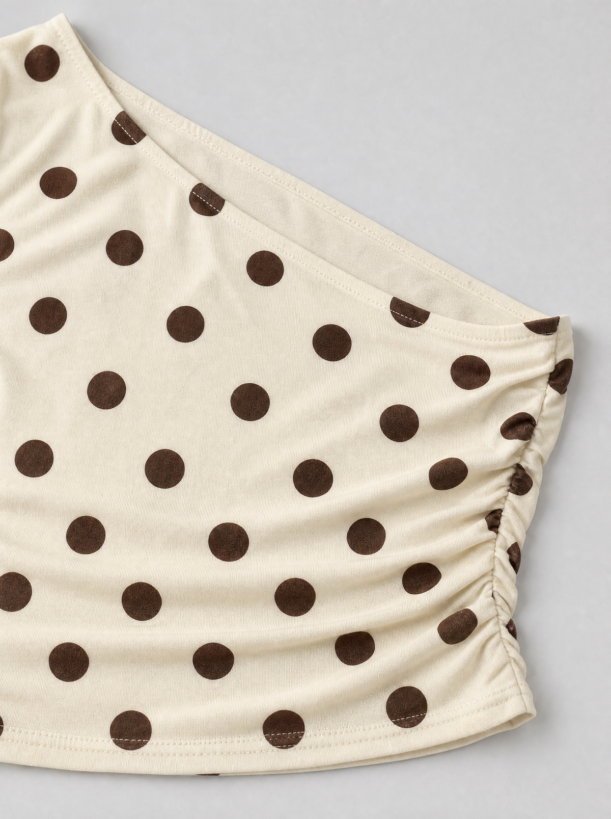 Close up of the asymmetric neckline and brown polka dot print on a cream top