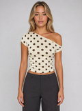 Woman wearing a cream polka dot one shoulder top, front view on a light grey studio background