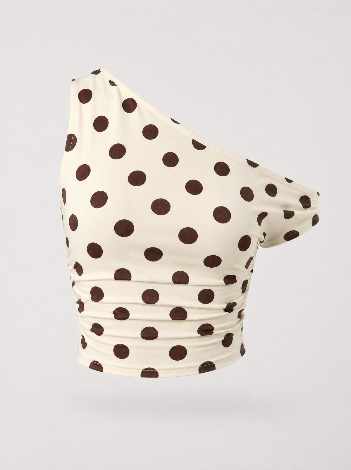Cream polka dot one shoulder top shown on its own against a light grey background