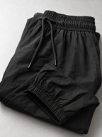 Close up of the drawstring waistband and elasticated ankle cuff on black parachute pants