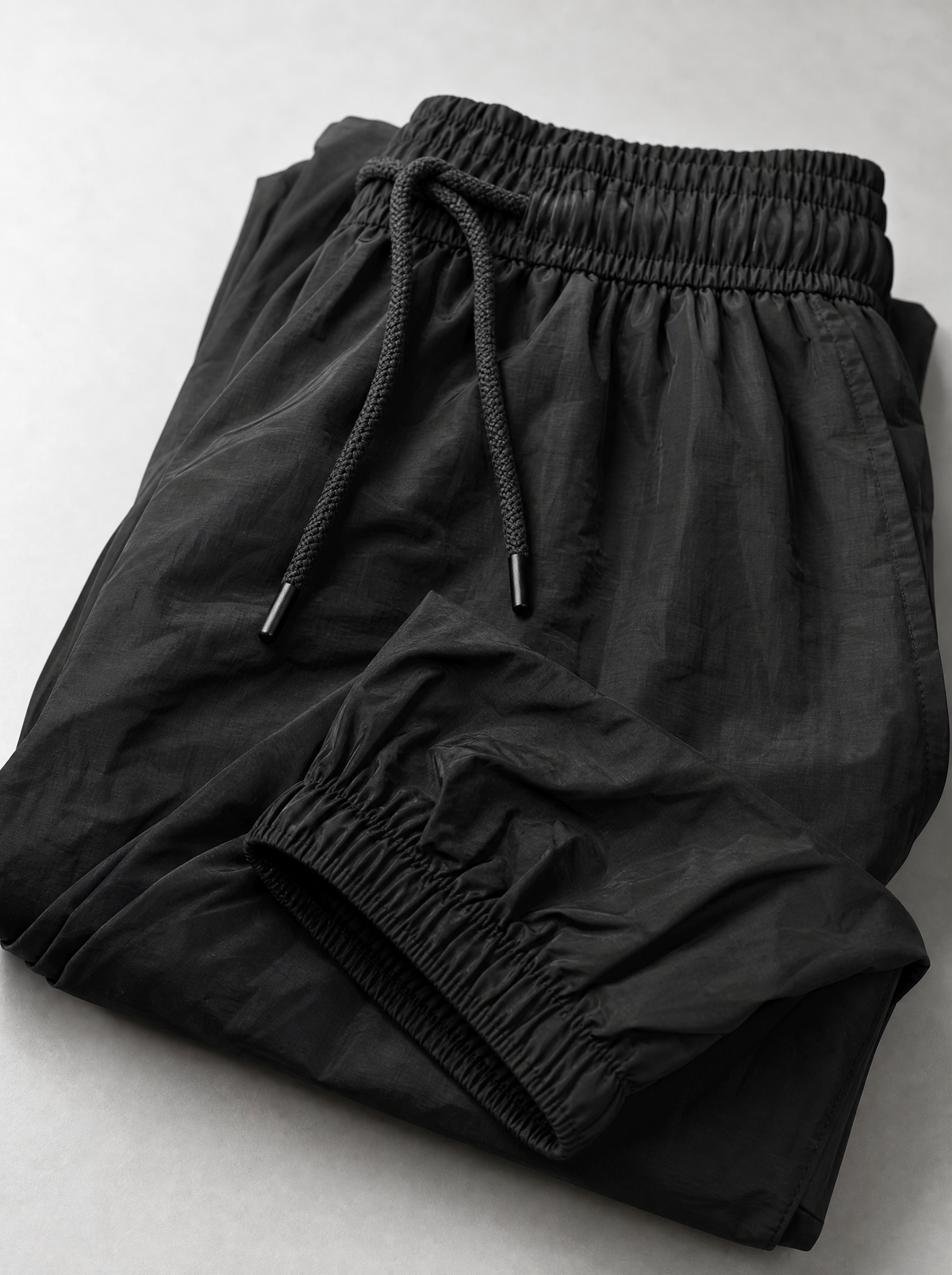 Close up of the drawstring waistband and elasticated ankle cuff on black parachute pants