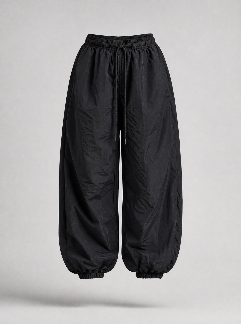 Black parachute pants with cuffed hem shown on their own against a light grey background