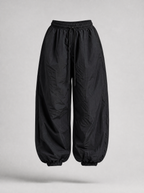 Black parachute pants with cuffed hem shown on their own against a light grey background
