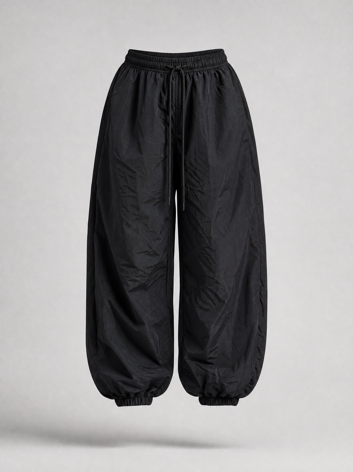 Black parachute pants with cuffed hem shown on their own against a light grey background