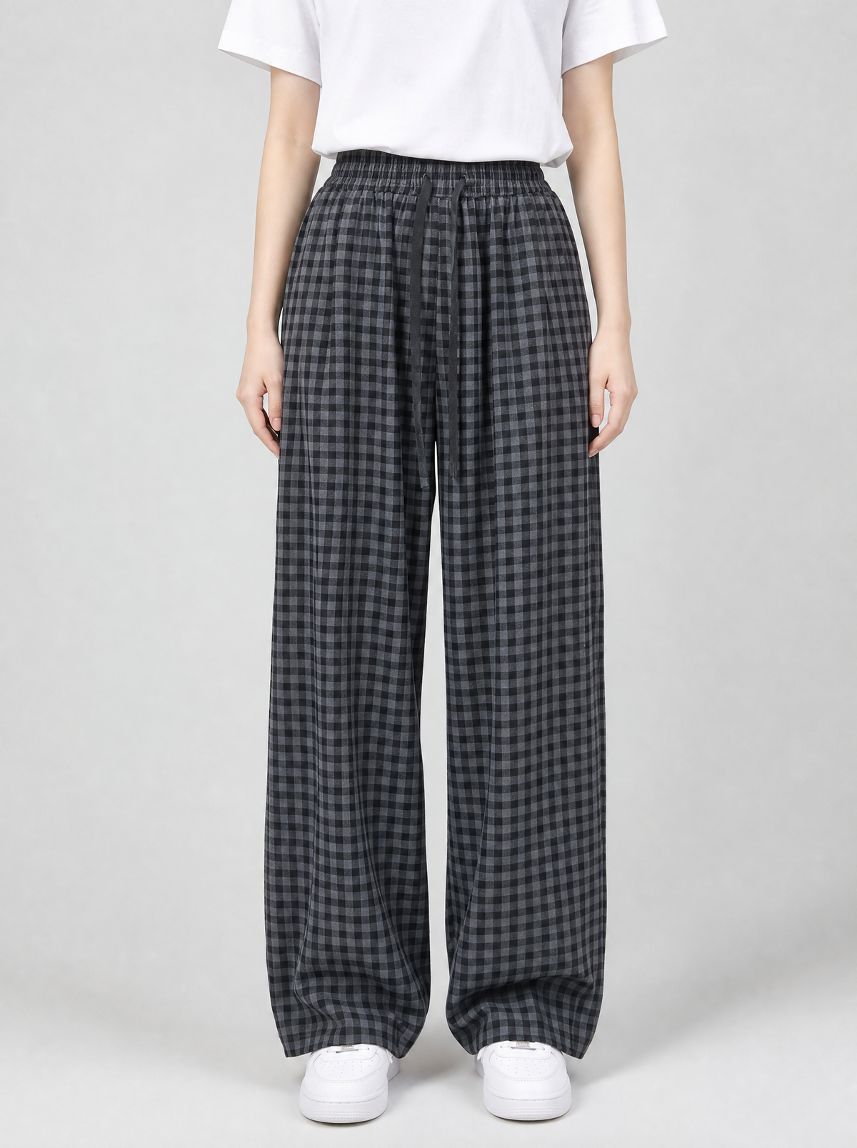 Woman wearing black check wide leg pants, front view on a light grey studio background