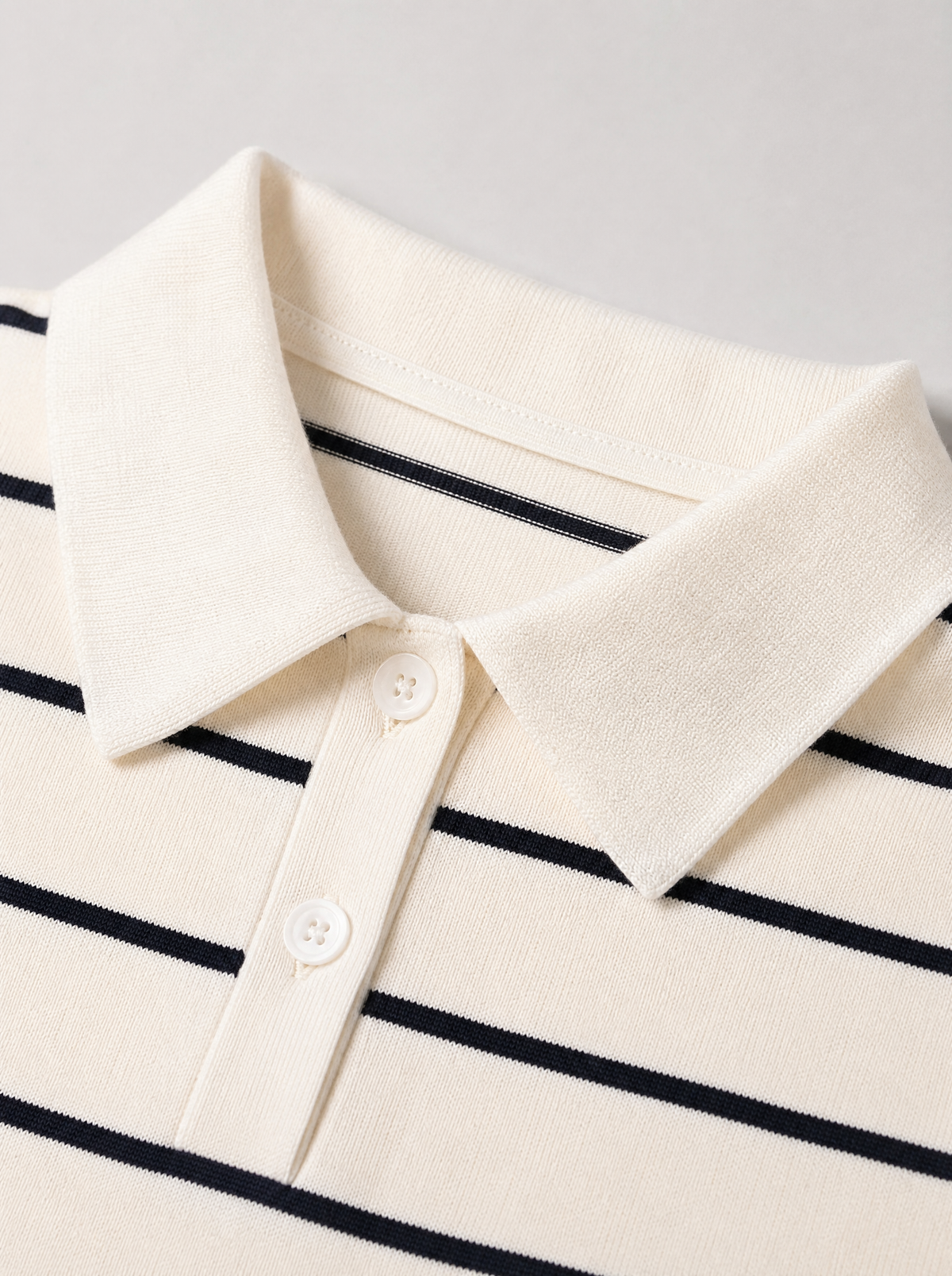 Close up of the pointed knit collar and thin navy stripe on a cream knit polo