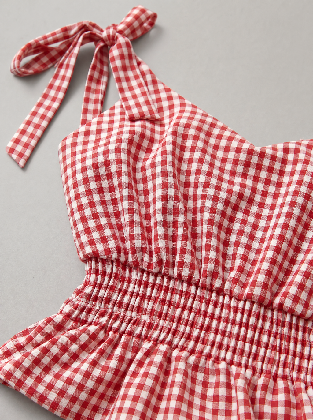 Close up of the tie shoulder strap and gingham check on a red peplum top