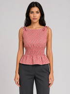 Woman wearing a red gingham tie shoulder peplum top, front view on a light grey studio background