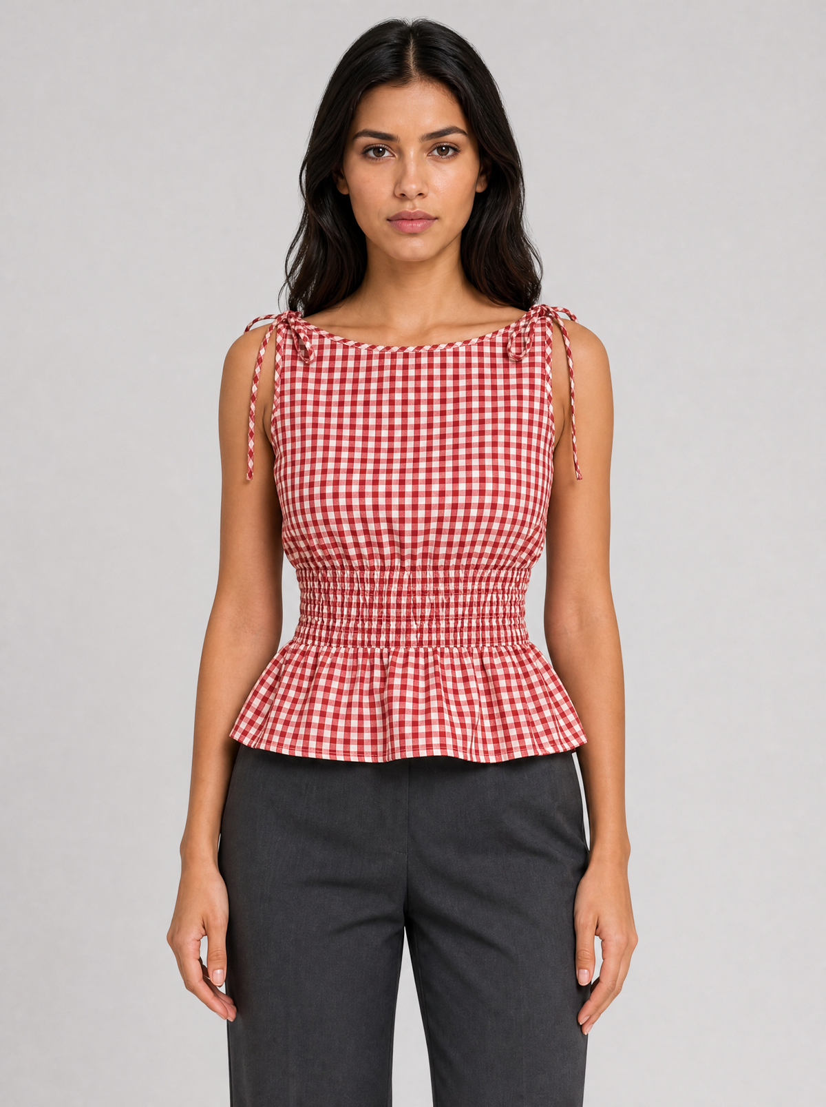 Woman wearing a red gingham tie shoulder peplum top, front view on a light grey studio background