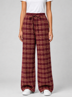 Woman wearing burgundy plaid wide leg pants, front view on a light grey studio background