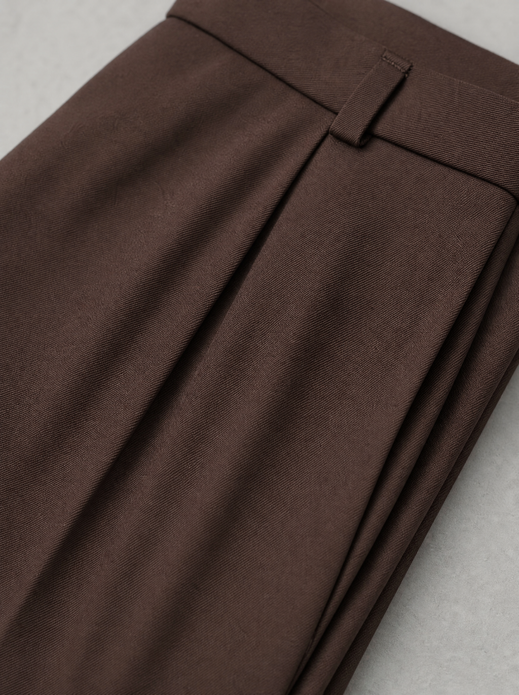 Close up of the waistband, belt loop and front pleat on brown tailored trousers