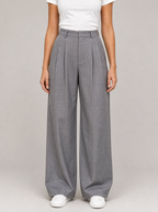 Woman wearing grey pleated high waist wide leg trousers, front view on a light grey studio background