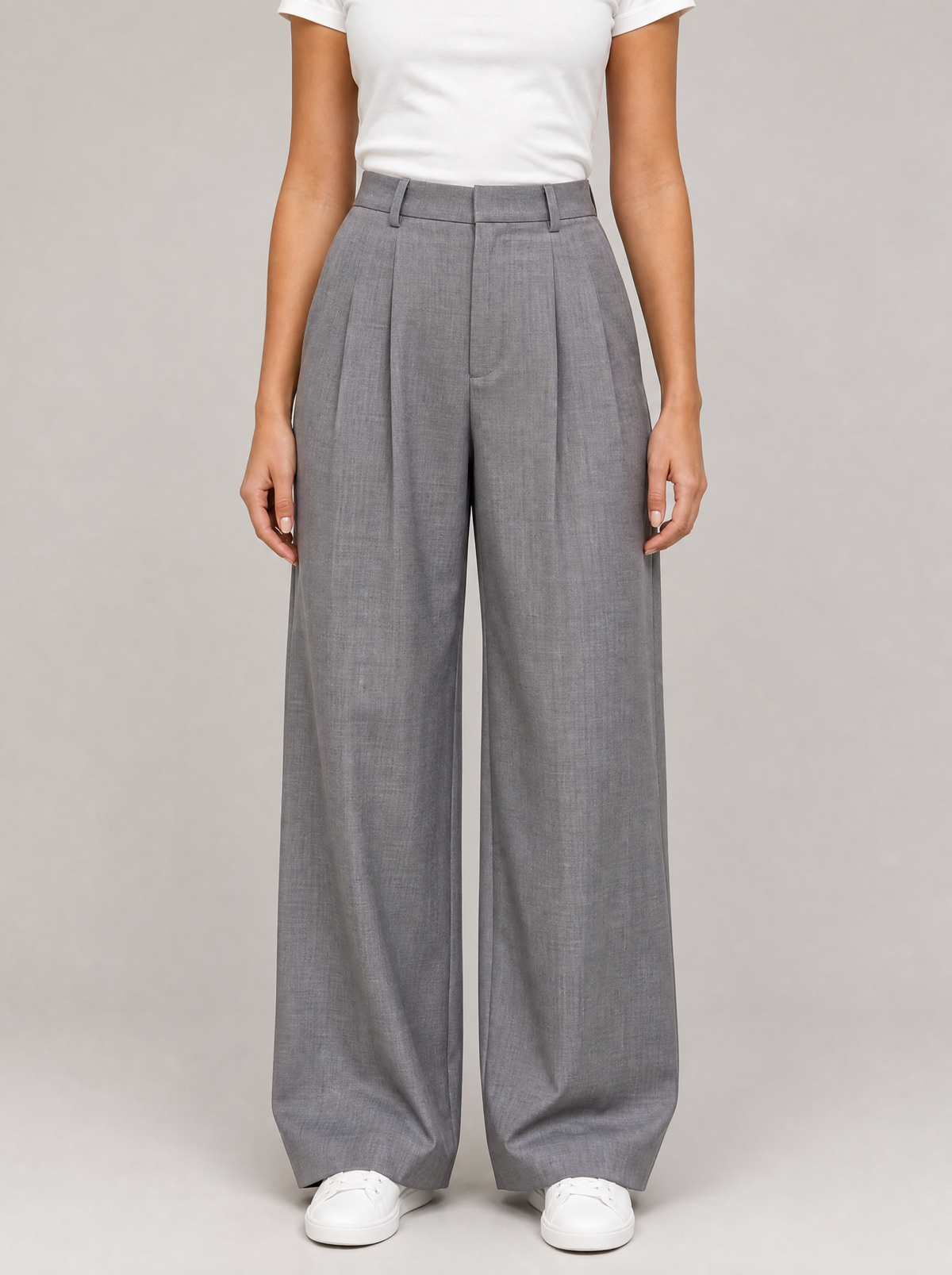 Woman wearing grey pleated high waist wide leg trousers, front view on a light grey studio background