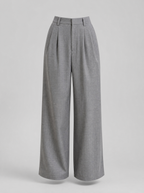 Grey pleated wide leg tailored trousers shown on their own against a light grey background