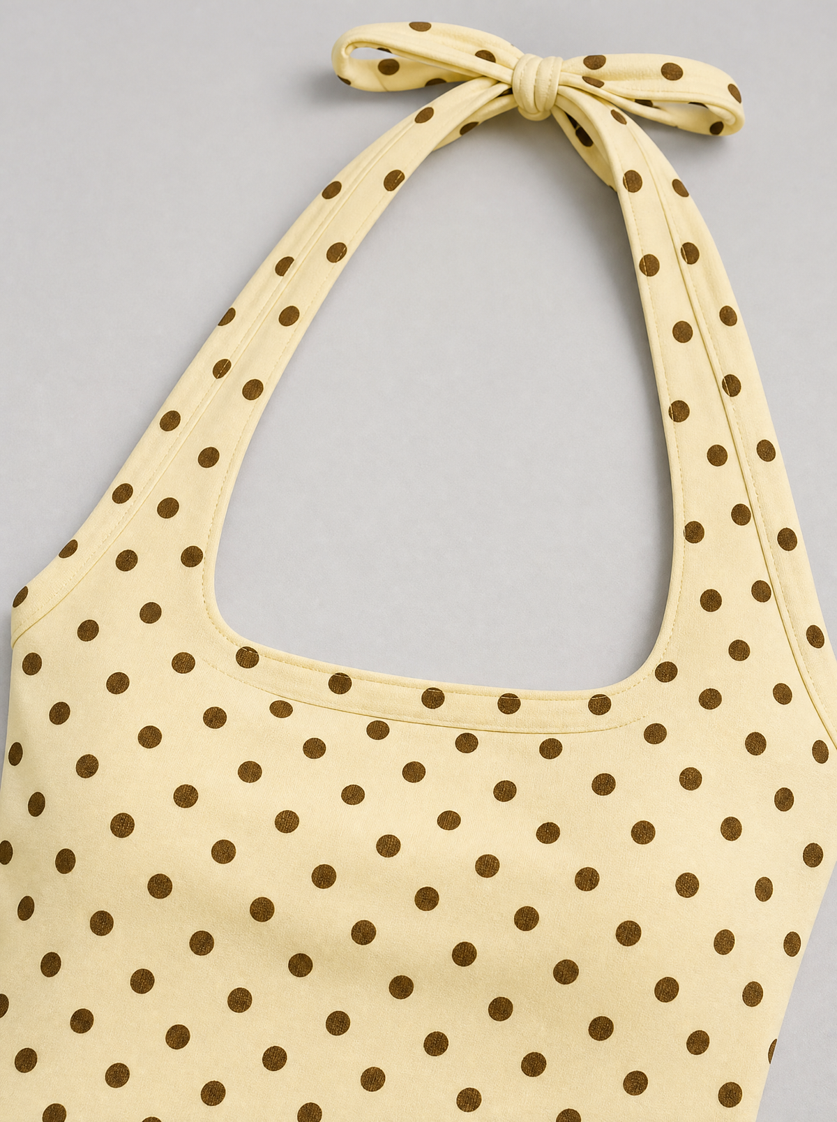 Close up of the square neckline and brown polka dot print on a yellow halter top