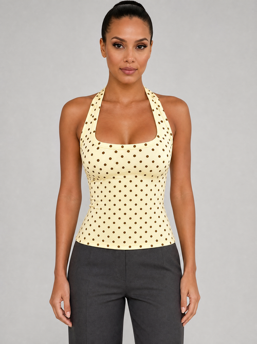 Woman wearing a yellow polka dot halter top, front view on a light grey studio background