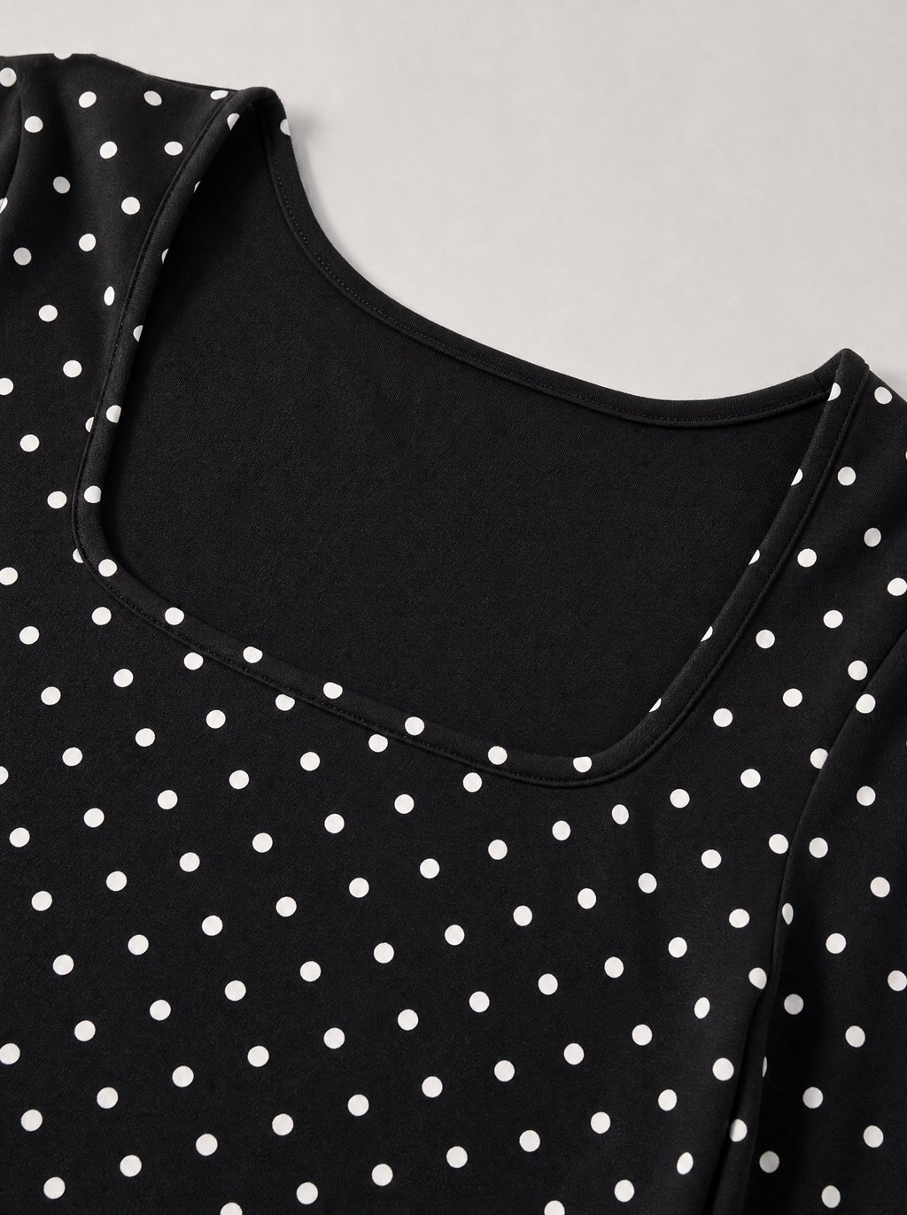 Close up of the square neckline and white polka dot print on a black jersey top