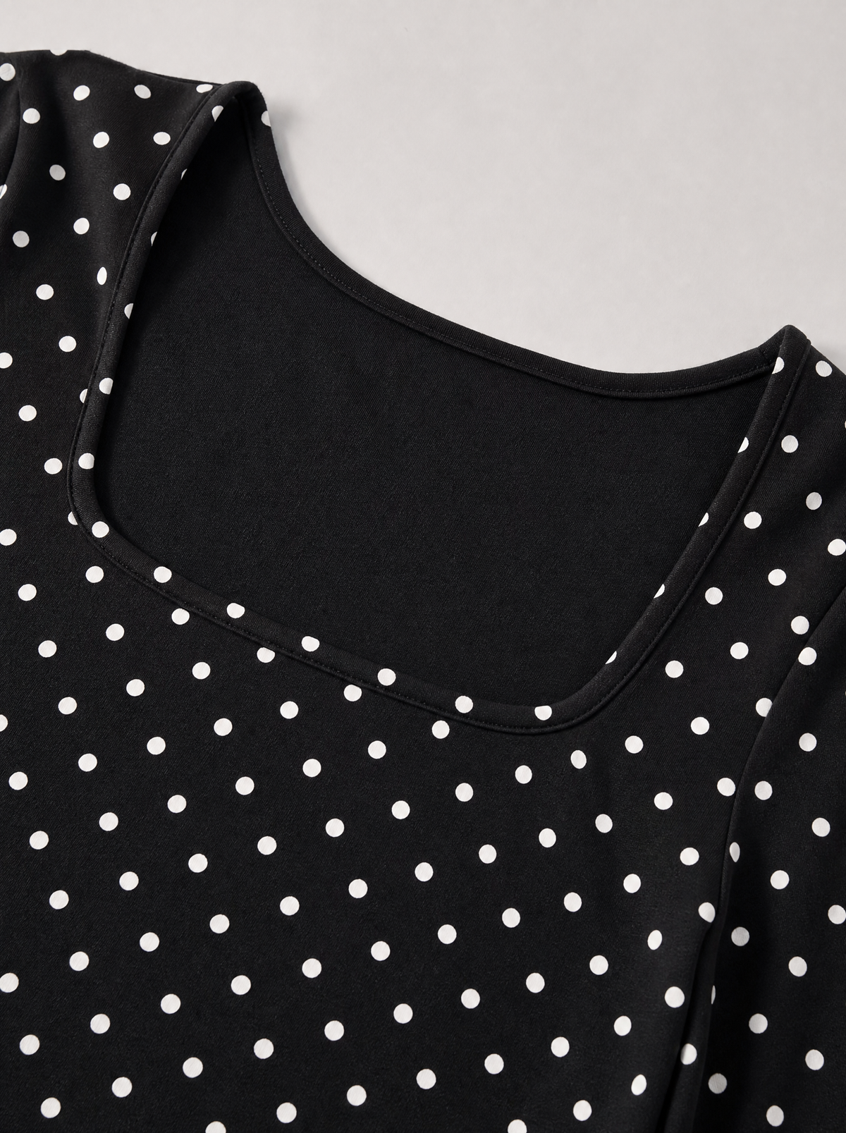 Close up of the square neckline and white polka dot print on a black jersey top