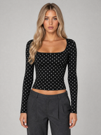 Woman wearing a black polka dot square neck long sleeve top, front view on a light grey studio background