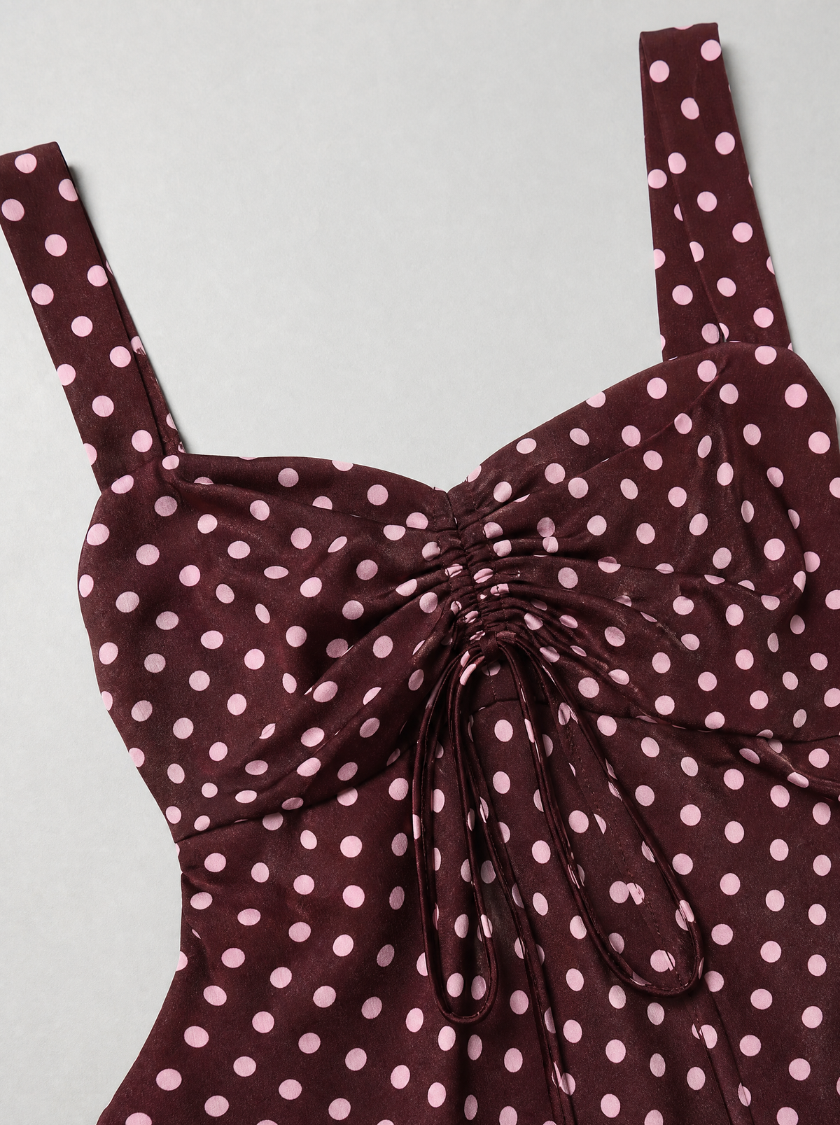 Close up of the drawstring ruching and polka dot print on a burgundy cami blouse