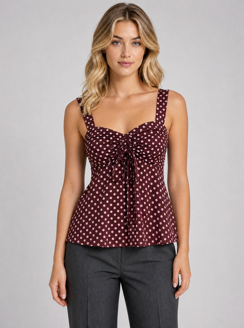Woman wearing a burgundy polka dot ruched cami blouse, front view on a light grey studio background