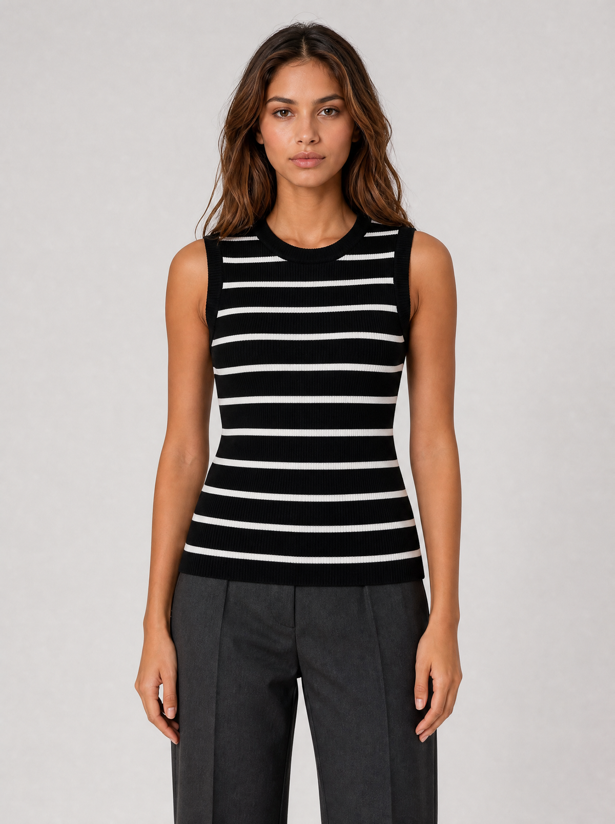 Woman wearing a black and white striped ribbed knit tank top, front view on a light grey studio background