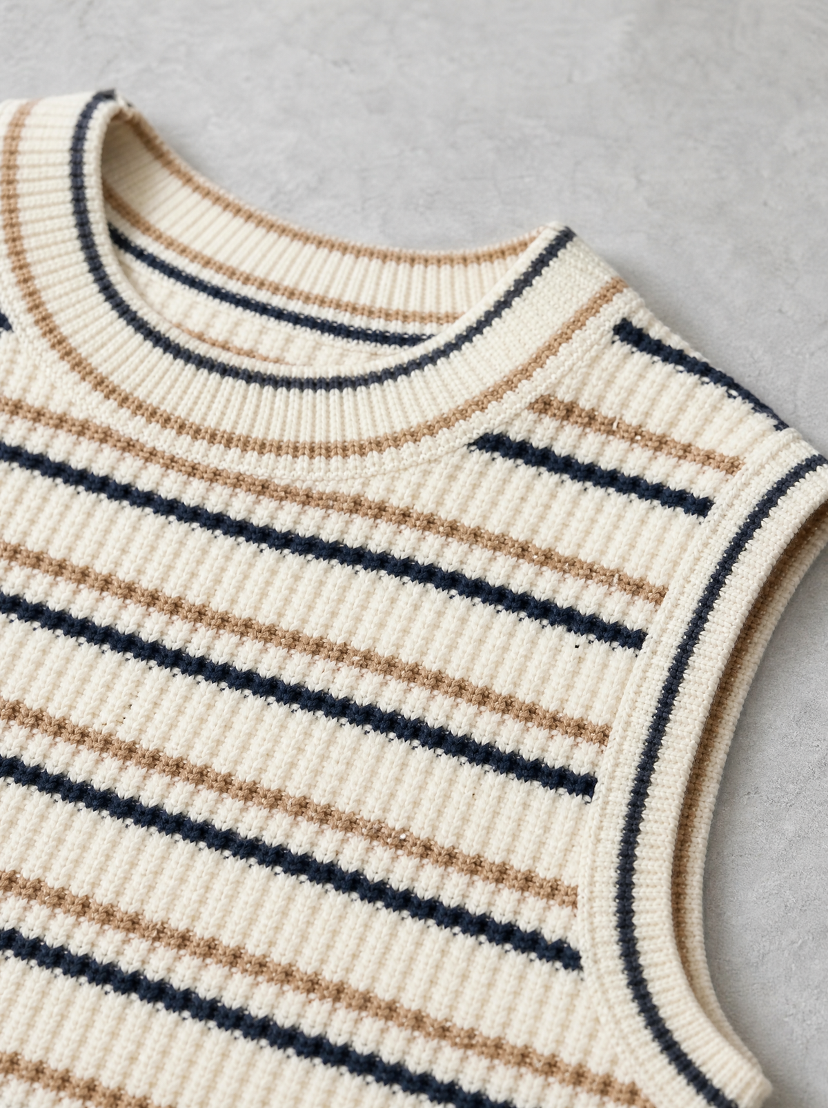 Close up of the ribbed crew neck and fine stripe knit on a cream sleeveless vest