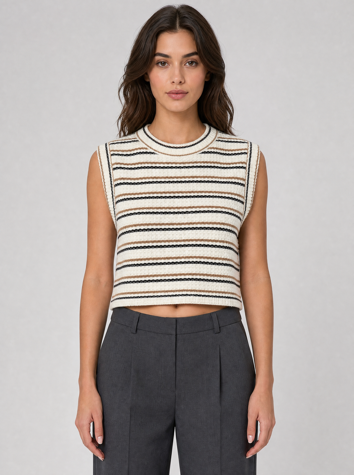 Woman wearing a cream striped sleeveless knit vest, front view on a light grey studio background