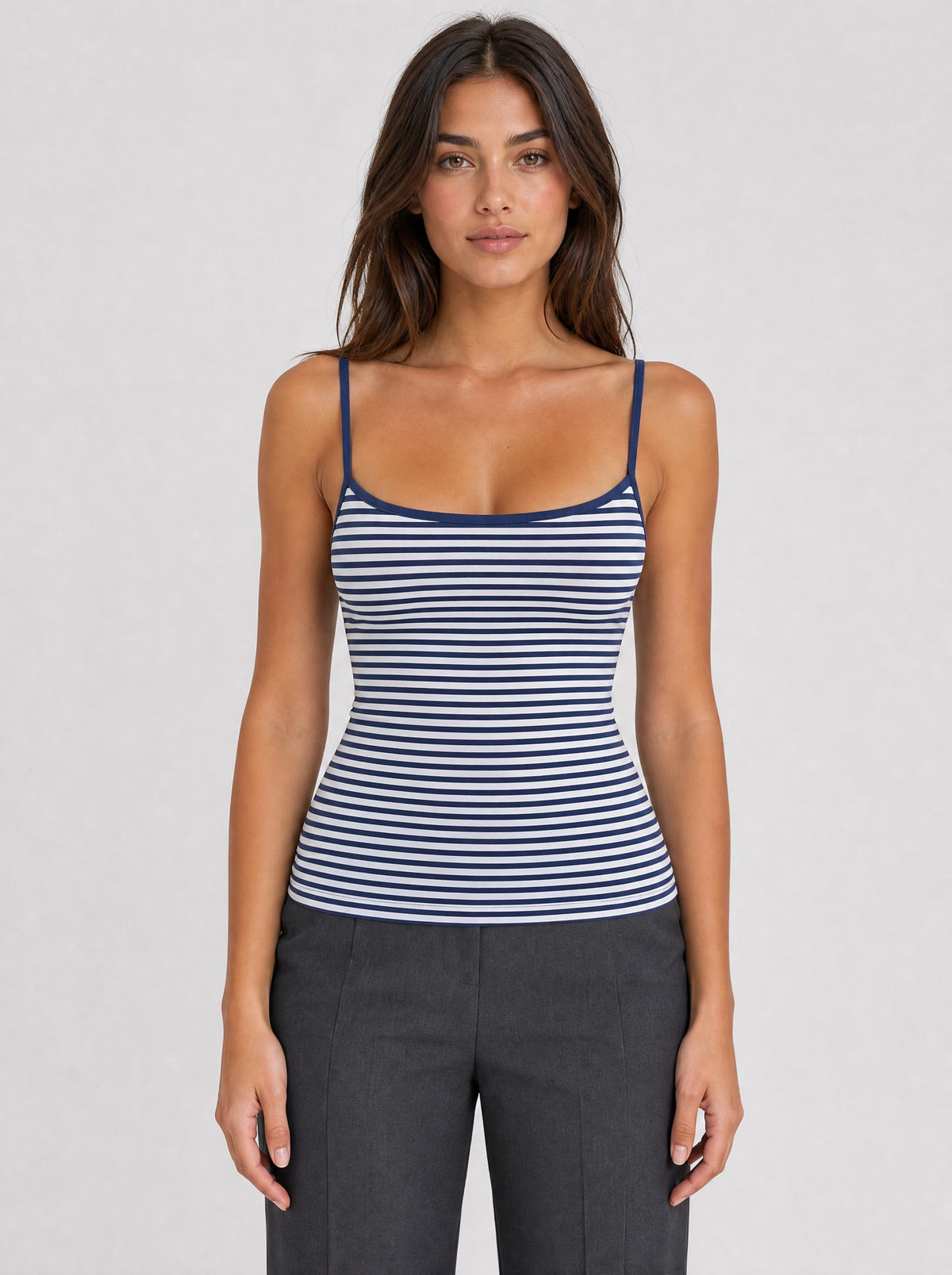 Woman wearing a navy striped thin strap cami top, front view on a light grey studio background