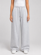Woman wearing grey wide leg fleece sweatpants, front view on a light grey studio background