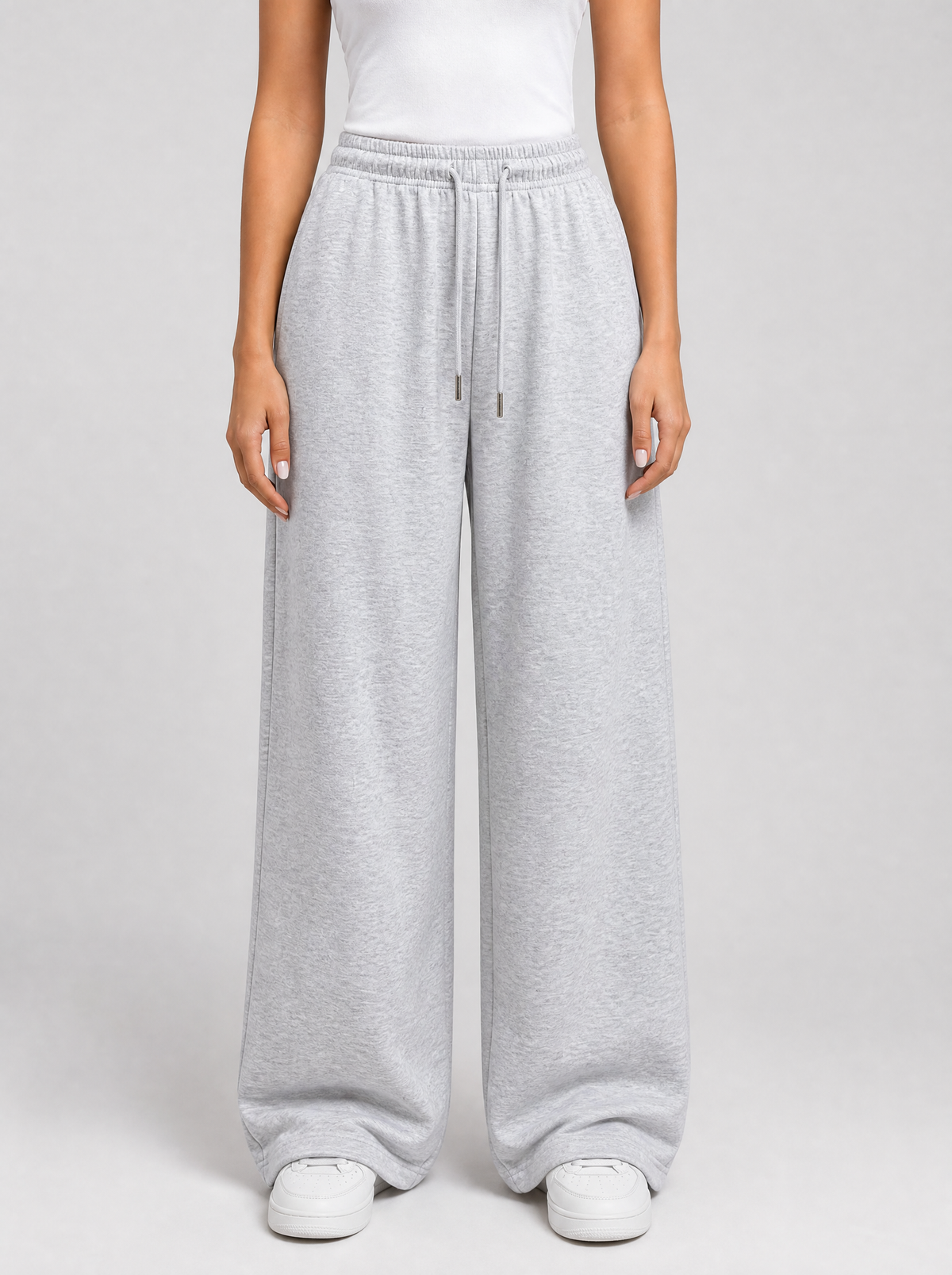 Woman wearing grey wide leg fleece sweatpants, front view on a light grey studio background